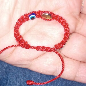 May include: Red string bracelet with a blue and white evil eye charm and a small silver charm.