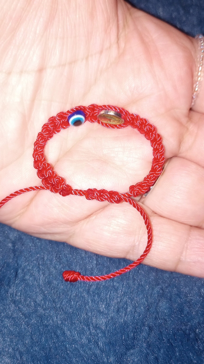May include: Red string bracelet with a blue and white evil eye charm and a small silver charm.