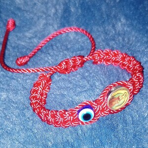 May include: Red string bracelet with a blue evil eye charm and a gold charm with a religious image.