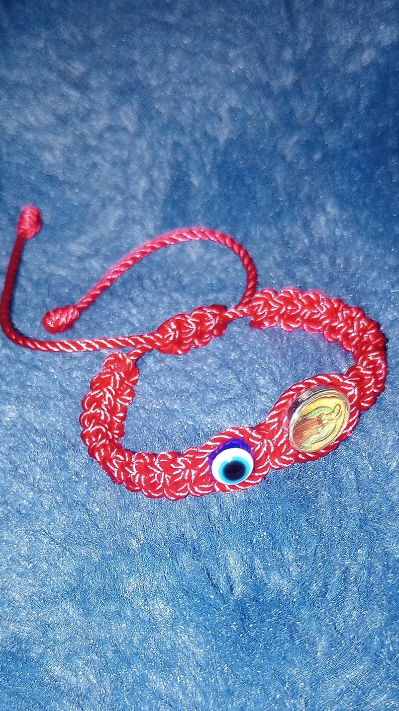 May include: Red string bracelet with a blue evil eye charm and a gold charm with a religious image.