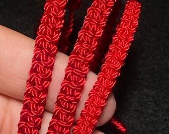 May include: Close-up of three strands of bright red, intricately woven cord. The cord has a textured, floral-like pattern, and is likely used for crafting or decorative purposes. The background is a dark, solid color, which makes the red cord stand out.