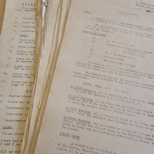 May include: Close-up of aged, yellowed paper documents with typed text and handwritten notes. The papers are stacked, showing details of hydraulic systems, including diagrams and technical specifications. The documents appear to be from the mid-20th century.
