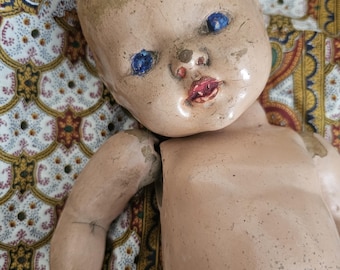 May include: A vintage porcelain doll with blue eyes and a painted smile. The doll is missing an arm and has a worn, aged appearance.