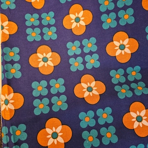 Puede incluir: Una tela azul con un patrón repetido de flores de cuatro pétalos de color naranja y blanco y flores de tres pétalos de color verde azulado.