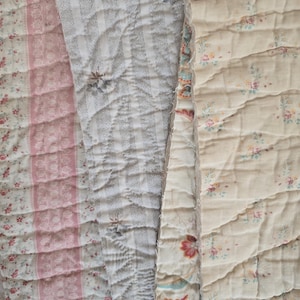 May include: Three strips of quilted fabric featuring distinct patterns. The left strip has pink floral bands, the centre strip displays grey and white vertical stripes with small floral accents, and the right strip shows a cream background with tiny floral prints.