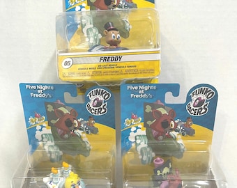 May include: Three Funko Racers die-cast vehicles from the Five Nights at Freddy's series. The toys are packaged in clear plastic with cardboard backings. The characters include Freddy, Chica, and Foxy the Pirate, each in a unique kart.