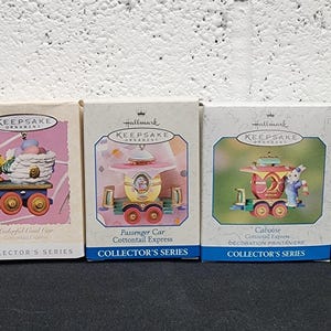 May include: Five Hallmark Keepsake ornaments in boxes. The boxes feature illustrations of train cars with various characters. The boxes are labeled "Collector's Series" and "Cottontail Express". The boxes are beige, pink, and blue.