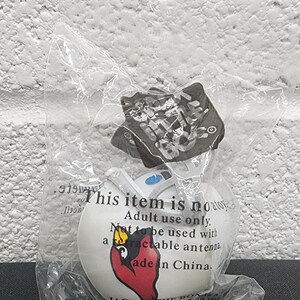 May include: A white spherical antenna topper featuring a red and black Jack in the Box character graphic. The item is sealed in a clear plastic bag with printed text that reads: This item is no toy. Adult use only. Not to be used with a retractable antenna. Made in China.