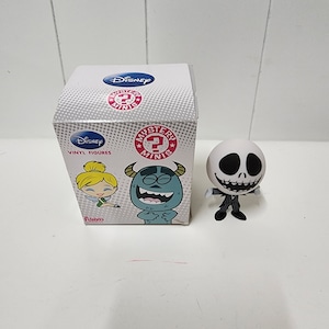May include: A white and black vinyl figure of Jack Skellington from the Nightmare Before Christmas movie. The figure is standing with its arms outstretched. The figure is packaged in a box with a Disney Mystery Minis logo and images of other characters from Disney movies.