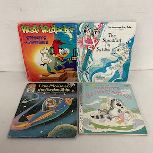 May include: Four children's books with colorful covers. The first book features Woody Woodpecker, the second book features a tin soldier, the third book features a mouse in a rocket ship, and the fourth book features a raccoon building a sandcastle.
