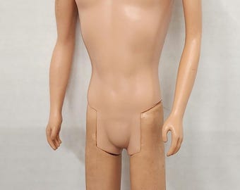 May include: A vintage doll with a tan complexion, blue eyes, and short brown hair. The doll is nude, with articulated arms and legs. The doll is standing against a white background.