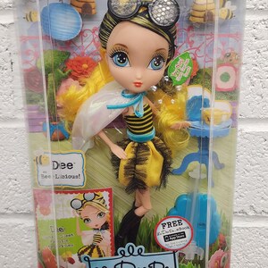 May include: A La Dee Da doll named Dee, in a clear plastic package. Dee is dressed in a bee-themed outfit with yellow hair and glasses. The packaging includes the text "Garden Tea Party".