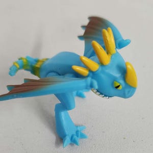 May include: A blue and yellow plastic dragon figurine with brown wings. The dragon has a spiky head and a toothy grin.