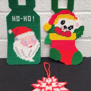 May include: Three handmade Christmas ornaments. One is a green tag with "HO-HO!" and a Santa face. Another is a red, yellow, and green elf in a stocking. The last is a red and white starburst.