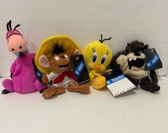 May include: Four plush toys featuring Looney Tunes characters. Included are a pink Speedy Gonzales, a brown Speedy Gonzales, a yellow Tweety Bird, and a brown Tasmanian Devil. Each toy has a tag that reads "Warner Bros. Studio Store BEAN BAG."