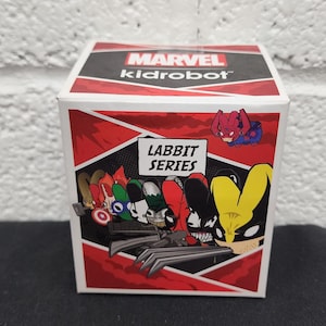 May include: A Marvel Kidrobot Labbit Series box featuring various Marvel characters. The box is white with red and black accents, and the Labbit Series logo is prominently displayed. A small Spider-Man figure is attached to the top.