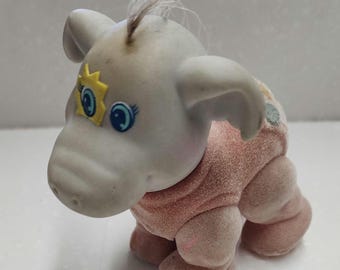 May include: A vintage, light gray elephant figurine with a pink velvet body. The elephant has blue eyes, a yellow star, and a tuft of hair. The figurine is a collectible toy.