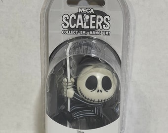 May include: A black and white plastic figure of Jack Skellington from the movie "The Nightmare Before Christmas" holding a pole. The figure is packaged in a clear plastic blister pack with a white card that reads "NECA SCALERS COLLECT 'EM, HANG 'EM!" and "Disney Tim Burton's The Nightmare Before Christmas".
