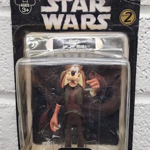 May include: A Star Wars action figure featuring Goofy as Jar Jar Binks, packaged in a clear plastic case. The packaging includes the Star Wars logo, the text "Goofy Jar Jar Binks", and a warning about small parts.