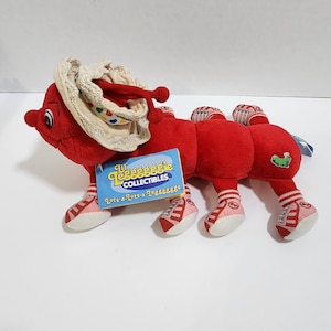 May include: Red plush caterpillar toy wearing a white hat with colorful polka dots and pink shoes with red stripes. The toy is labeled "Lil' Legga-Legga Collectibles. Lots-a-Lots-a-Legga-Legga!"