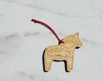 Puede incluir: Adorno de madera de caballo Dala con una cuerda roja para colgar. El caballo marrón claro presenta diseños florales y de corazón grabados. Un artículo tradicional de arte popular escandinavo.