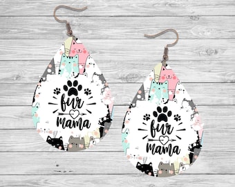 Könnte beinhalten: Ein Paar weiße tropfenförmige Ohrringe mit einem Katzen- und Pfotenabdruck-Design. Die Ohrringe zeigen den Text "fur mama" mit einem Herzen und einem Pfeil.