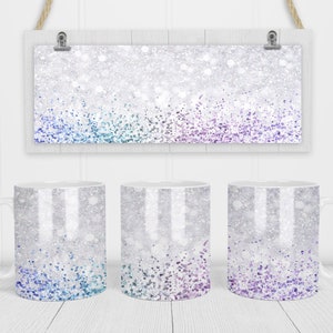 Op de afbeelding: Drie witte keramische mokken met een zilveren glitterachtergrond en een gradiënt van blauwe, turquoise en paarse glitter aan de onderkant.