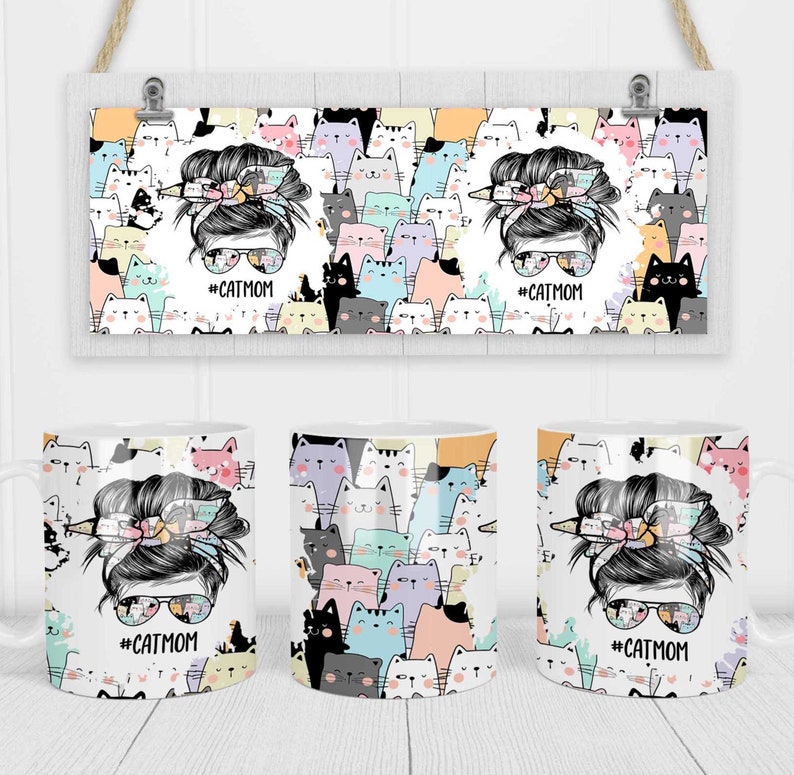 May include: White ceramic mug with a colorful design of cats and a woman with a messy bun and sunglasses. The text '#CATMOM' is printed on the mug.