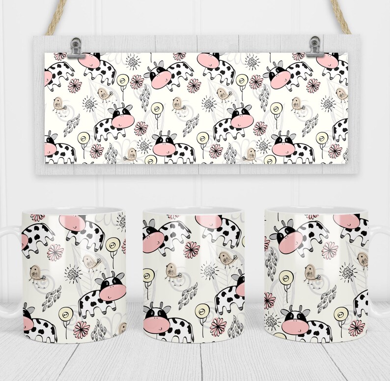 Op de afbeelding: Drie witte keramische mokken met een zwart-witte koe en bloemenpatroon. De mokken staan op een wit houten oppervlak.