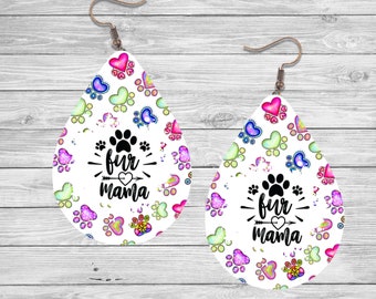 Könnte beinhalten: Ein Paar weiße tropfenförmige Ohrringe mit einem bunten Pfotenabdruck- und Herzmuster. Die Ohrringe haben einen silbernen Haken und den Text "fur mama" mit einem Pfeil und einem Herzen.