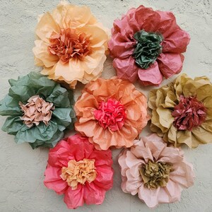 May include: Seven tissue paper flowers in various colours, including peach, pink, red, and green. The flowers are arranged in a circle on a light grey background.