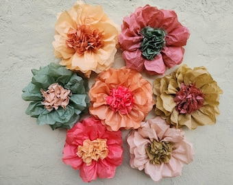 May include: Seven tissue paper flowers in various colors, including peach, pink, red, and green. The flowers are arranged in a circle on a light gray background.