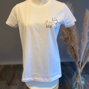 May include: White t-shirt with a black graphic of a wine glass and the text "partner in wine KATHY".