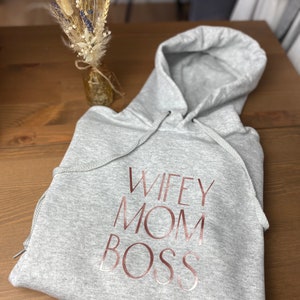 May include: Gray hooded sweatshirt with the text "WIFEY MOM BOSS" printed in rose gold.