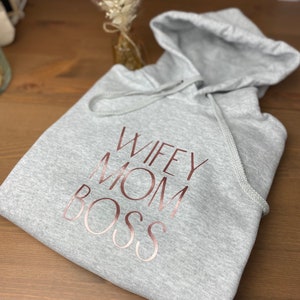 May include: Gray hooded sweatshirt with the words "Wifey Mom Boss" printed in rose gold.