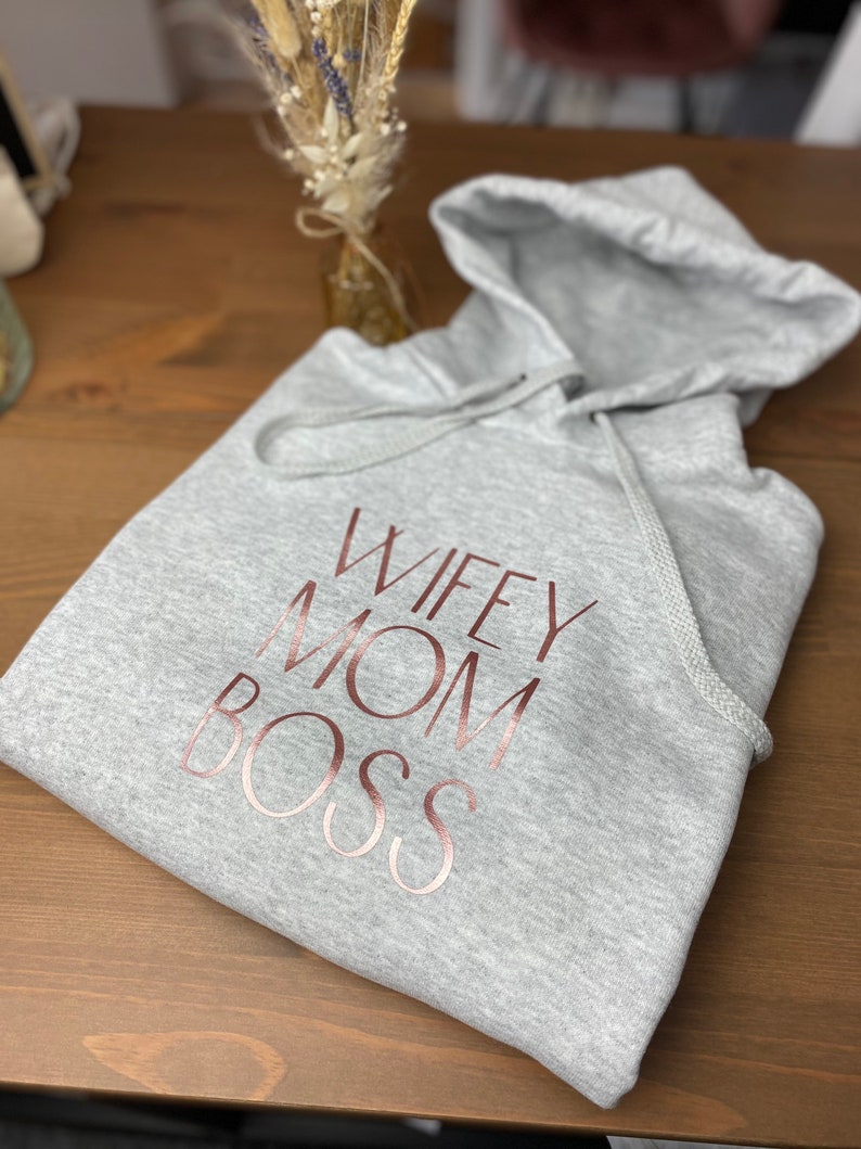 May include: Gray hooded sweatshirt with the words "Wifey Mom Boss" printed in rose gold.