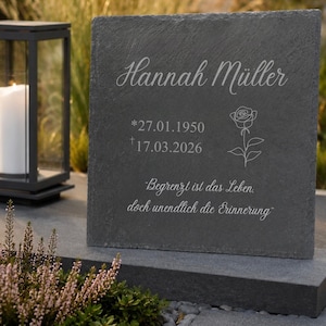 Könnte beinhalten: Ein dunkelgrauer Gedenkstein mit dem Namen "Hannah Müller", Daten und einer Rosenillustration. Die Inschrift lautet "Begrenzt ist das Leben, doch unendlich die Erinnerung". Eine Kerzenlaterne und Pflanzen befinden sich im Hintergrund.