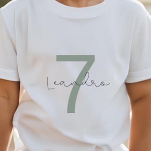 Könnte beinhalten: Weißes T-Shirt mit einer großen grünen Zahl 7 und dem Namen Leandro darunter in Kursivschrift.