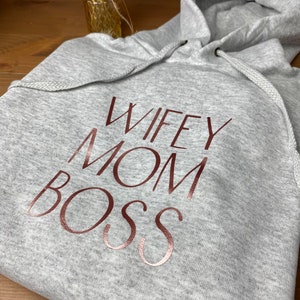 May include: Gray hooded sweatshirt with the text "Wife Mom Boss" in rose gold lettering.