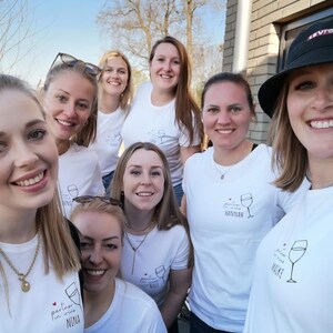 May include: A group of women wearing white t-shirts with the text "partner in wine" and their names. The women are smiling and looking at the camera.