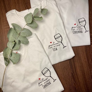 May include: Three white t-shirts with a wine glass graphic and the text "partner in wine" followed by a name. The names are Corinna, Lisa, and Janina.