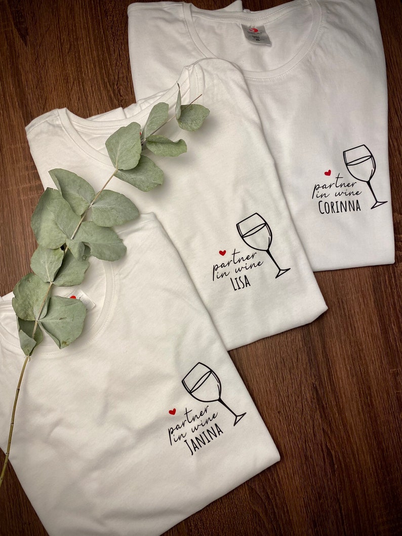 May include: Three white t-shirts with a wine glass graphic and the text "partner in wine" followed by a name. The names are Corinna, Lisa, and Janina.