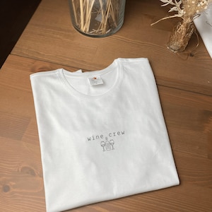 May include: White t-shirt with the text "wine crew" and a graphic of a wine bottle and four wine glasses.