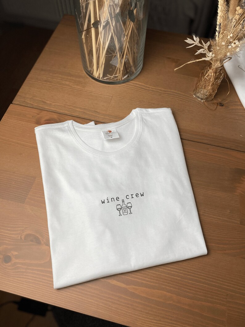 May include: White t-shirt with the text "wine crew" and a graphic of a wine bottle and four wine glasses.