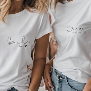 Könnte beinhalten: Zwei weiße T-Shirts mit schwarzem Text. Das erste Shirt sagt "bride to be" mit einem kleinen Herzen. Das zweite Shirt sagt "crew to drink" mit zwei Champagnergläsern.