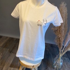 May include: White t-shirt with a black and red graphic that says "partner in wine Kathy" with a red heart and a drawing of a wine glass.