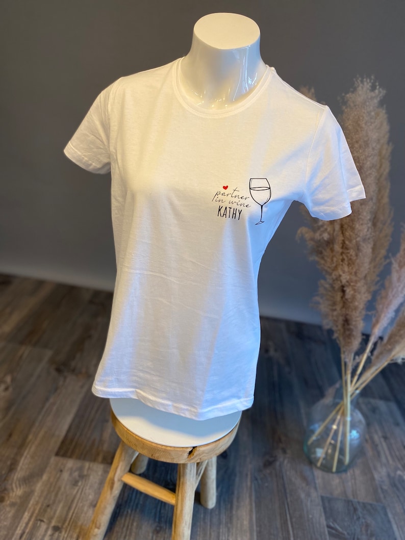 May include: White t-shirt with a black and red graphic that says "partner in wine Kathy" with a red heart and a drawing of a wine glass.
