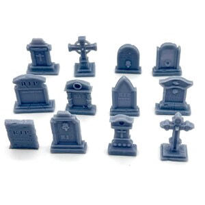 May include: A selection of miniature grey gravestones in diverse forms. Some have crosses, others bear the inscription "RIP". These small, detailed gravestones are likely intended for a tabletop game or diorama, with intricate designs.