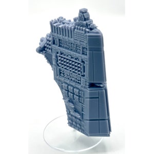 May include: A grey miniature spaceship model with detailed architectural features. The model includes rectangular windows, gridded sections, and texturing. It is mounted on a clear, circular stand, highlighting its design.