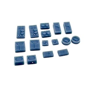 May include: A selection of small, dark grey plastic model components, including rectangular and circular shapes with detailed surface features. The pieces vary in size and design, suggesting they are parts of a larger model or project.